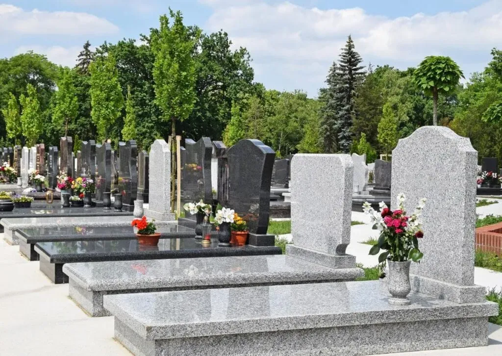 Alignement de monuments funéraires et pierres tombales en granit dans un cimetière paysager.