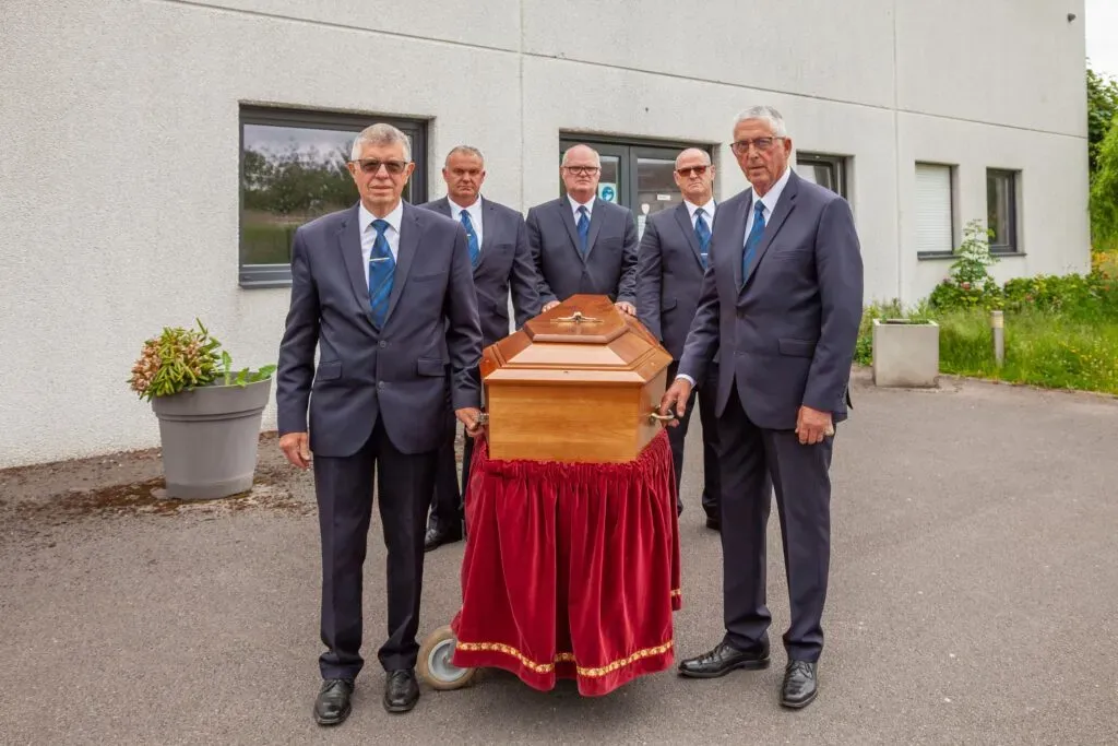 Porteurs funéraires professionnels entourant un cercueil placé sur un chariot de transport.