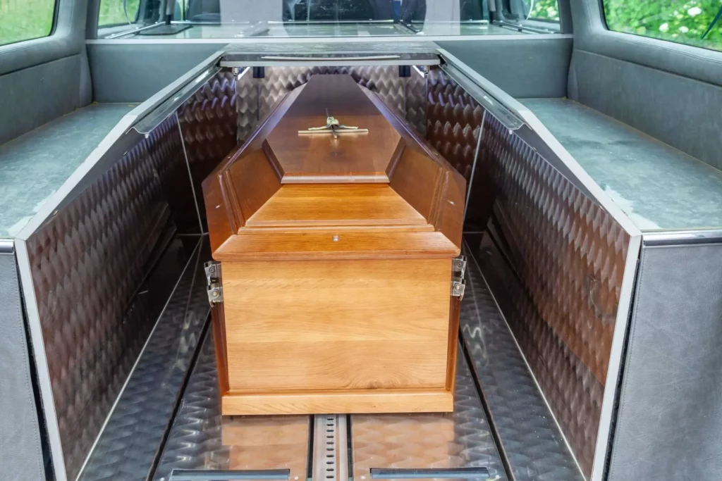 Cercueil en bois avec poignée et ornement, installé dans le coffre d'un corbillard.
