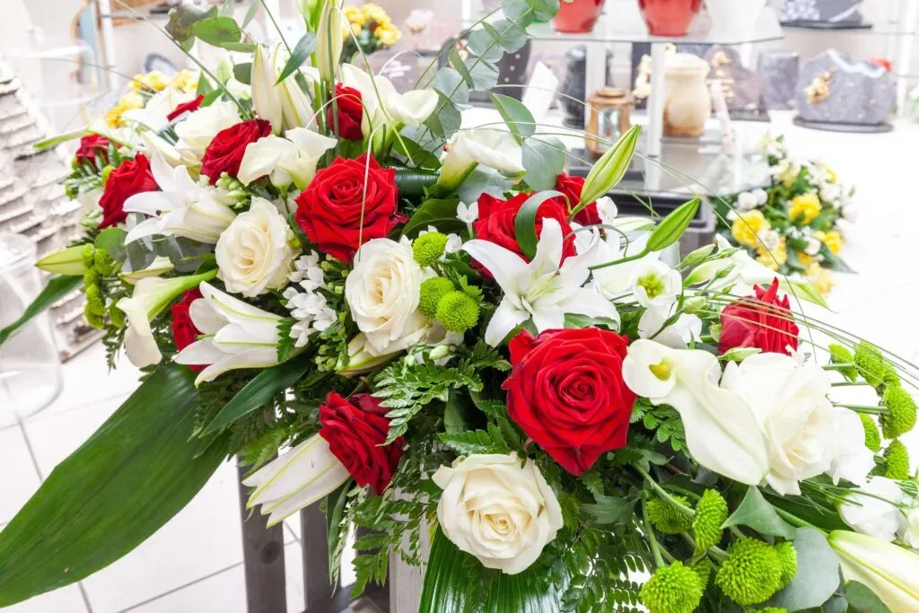 Composition florale funéraire garnie de roses rouges, de lys blancs et de feuillage vert.